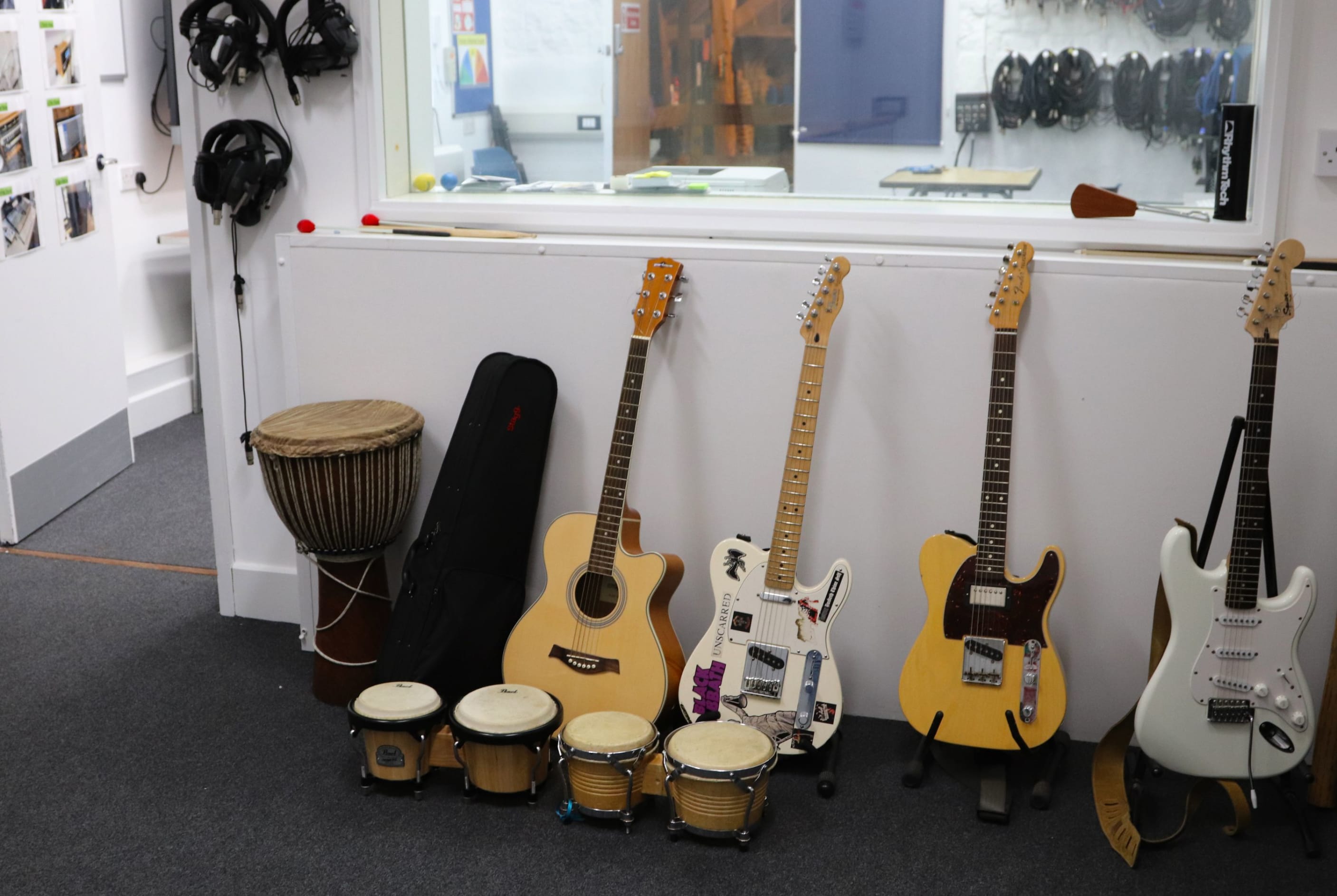 The recording studio at the Orpheus cenre in Godstone, Surrey. Four guitars are on stands agaist a wall, There are bongos on the floor in front. There are headphones and leads on hooks on the wall.